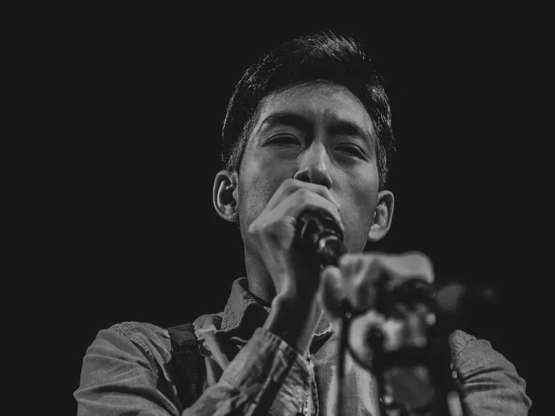 Black and white photo of Chris Le Nguyen singing into a microphone on stage